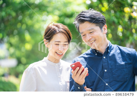 看智能手機的中年夫婦(夫婦,戶外,新鮮綠色,微笑) 看智能手機的中年夫婦(夫婦,戶外,新鮮綠色,微笑) 89638479