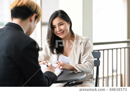 Two asian corporate businesspeople discussing business while sitting on a terrace outside office. Two asian corporate businesspeople discussing business while sitting on a terrace outside office. 89638573