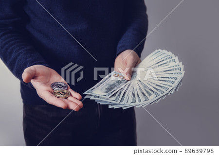 A man is holding a fan of hundred-dollar bills and two bitcoins 89639798