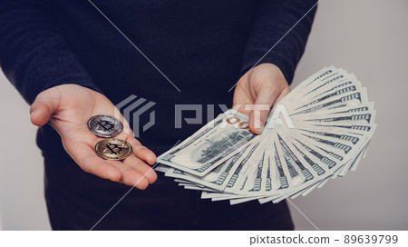 A man is holding a fan of hundred-dollar bills and two bitcoins 89639799