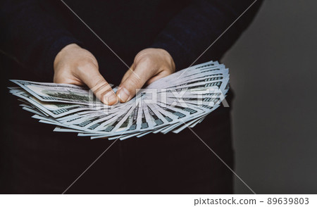 A man holds a fan of 100 dollar bills in his hands A man holds a fan of 100 dollar bills in his hands 89639803