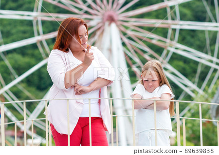 Family portrait. The mother shakes her finger at her daughter for her capricious behavior. Ferris wheel in the background. Concept of family holidays and summer vacations Family portrait. The mother shakes her finger at her daughter for her capricious behavior. Ferris wheel in the background. Concept of family holidays and summer vacations 89639838