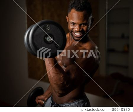 Attractive african american man smiling and doing exercise with dumbbells. Attractive african american man smiling and doing exercise with dumbbells. 89640580