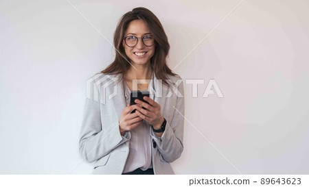 Businesswoman wearing glasses with mobile phone in hand standing in modern office 89643623