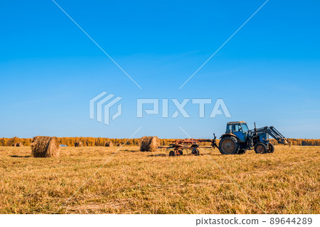 Tractor collecting haystacks in a field Tractor collecting haystacks in a field 89644289