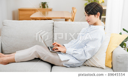一個年輕女子坐在沙發上使用電腦 89645554