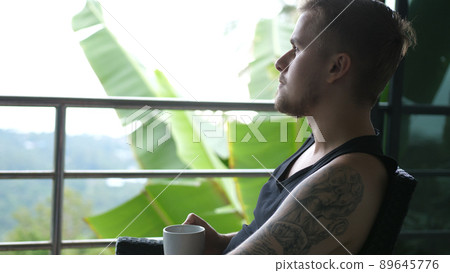 Young man drinking coffee sitting in balcony with exotic garden and sea view. 3840x2160 89645776