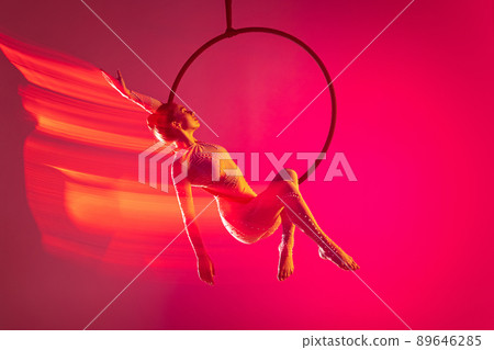 Young artistic girl, professional air gymnast training, performing isolated over pink background with mixed lights effect Young artistic girl, professional air gymnast training, performing isolated over pink background with mixed lights effect 89646285