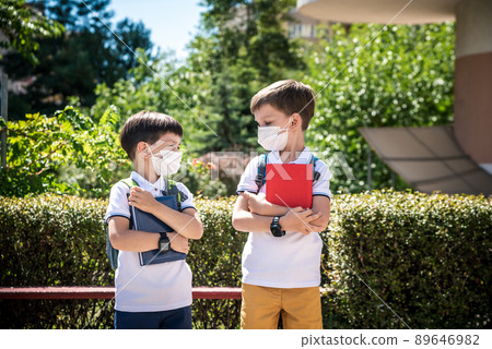 two boys, schoolchildren in black school uniforms with backpacks in a medical mask go to school independently, hold hands, friendship concept, study concept during coronavirus, back to school 89646982