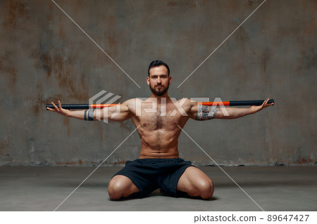 A ninja man holds on to a fighting stick and attacks close-up on gray studio background A ninja man holds on to a fighting stick and attacks close-up on gray studio background 89647427