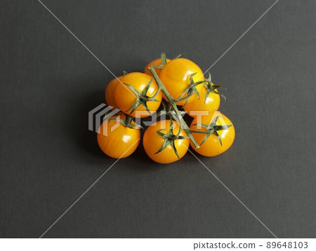 Isolated yellow cherry tomatoes on a branch on a dark background. 89648103