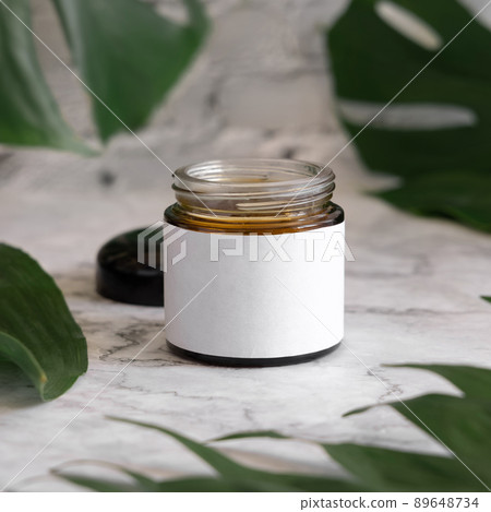 Brown jar and monstera leaves on marble table close up. Brand packaging mockup 89648734