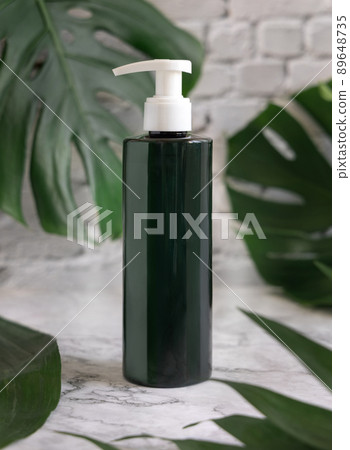 Dark green one pump dispenser and monstera leaves on marble table close up. Brand packaging mockup 89648735