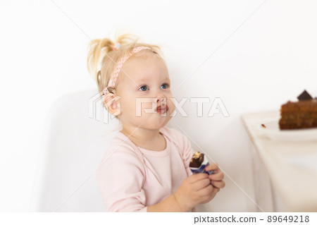 Baby with cochlear implant sitting at home and eating. Hear aid and medicine innovating technology concept Baby with cochlear implant sitting at home and eating. Hear aid and medicine innovating technology concept 89649218