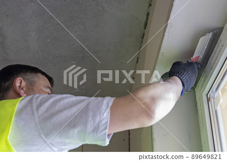 The master levels the wall with a spatula, applying the plaster mixture on the wall. 89649821