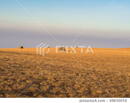 Haystacks in the distance in a golden field under a blue sky. Countryside Caucasian area. 89650058