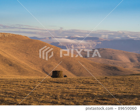 A rolled haystack in a field high in a mountain valley under a blue sky and low drifting clouds. The nature of the Caucasus A rolled haystack in a field high in a mountain valley under a blue sky and low drifting clouds. The nature of the Caucasus 89650060