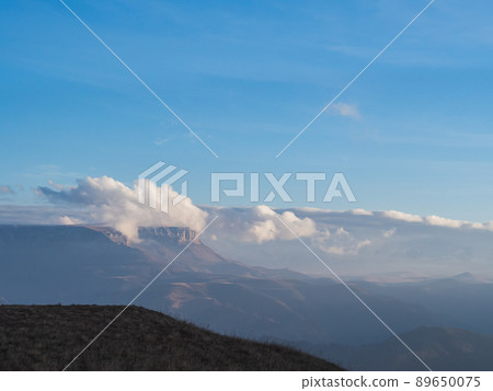 Hiding in the clouds under a bright blue sky is the Bermamyt plateau surrounded by a mountain valley on an autumn day Hiding in the clouds under a bright blue sky is the Bermamyt plateau surrounded by a mountain valley on an autumn day 89650075