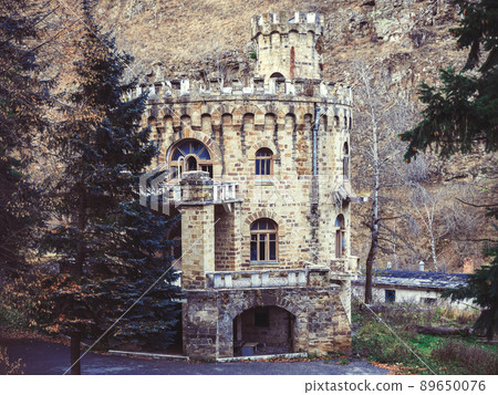 The abandoned castle stands in a forested area in a mountain valley. Government country house of the times of the USSR in the style of a fortress 89650076
