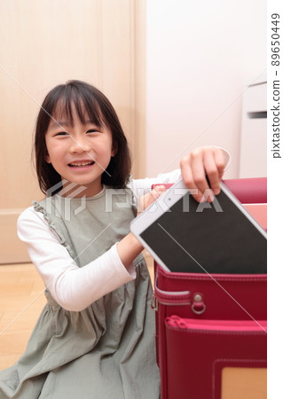 一個小學一年級的女孩從書包裡拿出平板電腦 89650449