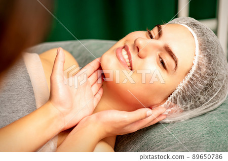 Plastic surgery and beauty concept. Professional cosmetician examining and touching the face of the beautiful young caucasian smiling woman in a clinic of esthetic cosmetology Plastic surgery and beauty concept. Professional cosmetician examining and touching the face of the beautiful young caucasian smiling woman in a clinic of esthetic cosmetology 89650786