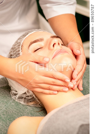 Facial treatment massage. Beautiful young caucasian woman with perfect skin receiving face and neck massage at a beauty spa Facial treatment massage. Beautiful young caucasian woman with perfect skin receiving face and neck massage at a beauty spa 89650787