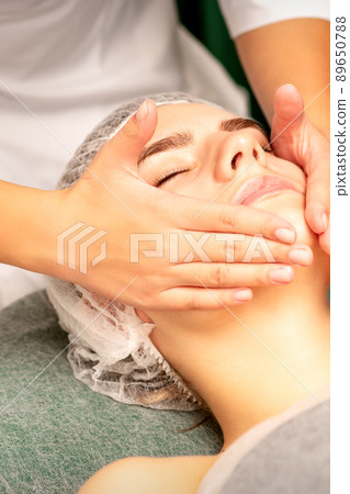 Facial treatment massage. Beautiful young caucasian woman with perfect skin receiving face and neck massage at a beauty spa Facial treatment massage. Beautiful young caucasian woman with perfect skin receiving face and neck massage at a beauty spa 89650788