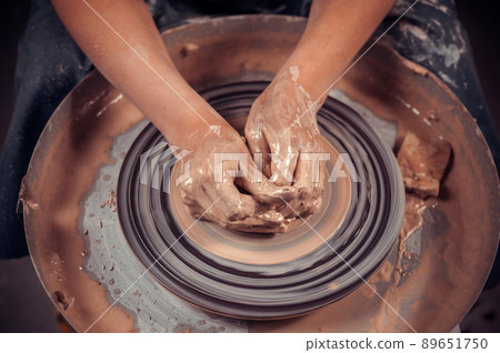 Hands of the master potter and vase of clay on the potter's wheel close-up. Master crock. Twisted potter's wheel. Hands of the master potter and vase of clay on the potter's wheel close-up. Master crock. Twisted potter's wheel. 89651750
