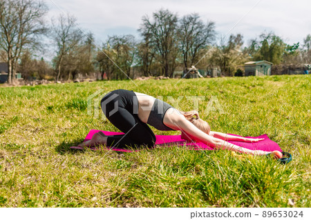 Portrait of a caucasian young fitness blonde girl doing yoga on yoga mat in nature at park Portrait of a caucasian young fitness blonde girl doing yoga on yoga mat in nature at park 89653024