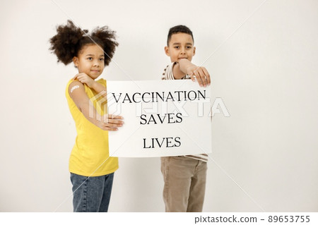Boy and girl standing isolated on white background. Children have a band-aid on their shoulders after vaccination. Poster said that vaccination saved lives. 89653755