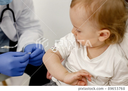 Cropped photo of a little boy in hospital. Medical worker wearing blue gloves and face mask. Boy wearing white t-shirt. 89653768
