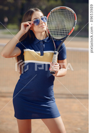 Tennis player woman holding a racket. Caucasian woman playing tennis on the court outdoors. Woman wearing blue sport dress and posing for a photo. 89653989