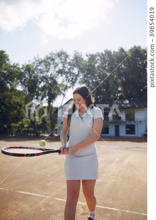 Tennis player woman focused during play. Caucasian woman playing tennis on the court outdoors. Woman wearing white sport dress. 89654019