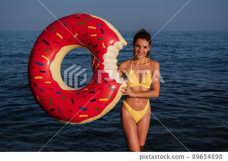 happy young woman with a sexy body in a swimsuit with an inflatable circle in her hands is resting on the sea happy young woman with a sexy body in a swimsuit with an inflatable circle in her hands is resting on the sea 89654898