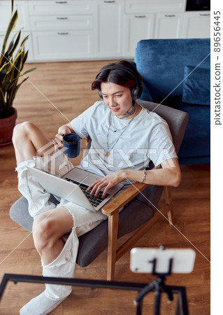 Asian guy working with laptop and listening to music with headphones Asian guy working with laptop and listening to music with headphones 89656445