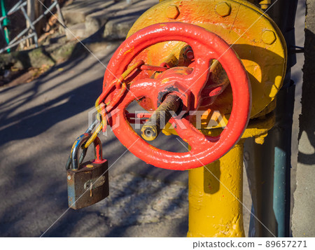 A metal red valve with a lock hanging from a chain on a yellow pipe. Closeup photo A metal red valve with a lock hanging from a chain on a yellow pipe. Closeup photo 89657271