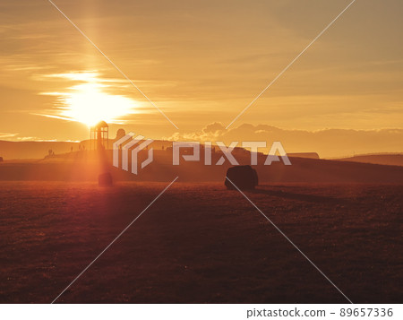 The outlines of fields and an observation tourist site in the highlands at the level of clouds in a haze under the bright rays of the setting sun The outlines of fields and an observation tourist site in the highlands at the level of clouds in a haze under the bright rays of the setting sun 89657336