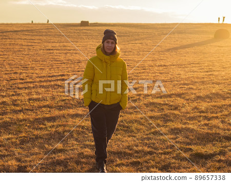 A woman walks through a golden field illuminated by the evening sun in the highlands at cloud level. Soft focus. A woman walks through a golden field illuminated by the evening sun in the highlands at cloud level. Soft focus. 89657338