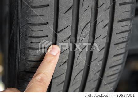 Mechanic pointing with hand at tyre wear indicator at car service center. Vehicle wheel protector control and inspection during maintenance. Tread wear check test inspection at automotive maintenance 89657391