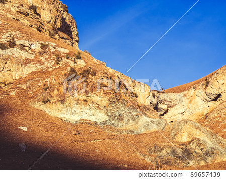 Steep autumn rocky mountains of caucasus with dry golden grass lit by sun under blue sky 89657439