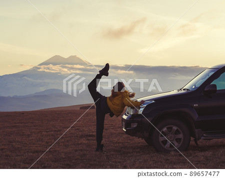 A woman makes a leg swing while standing by an SUV in an autumn high-mountain field against the backdrop of Elbrus A woman makes a leg swing while standing by an SUV in an autumn high-mountain field against the backdrop of Elbrus 89657477