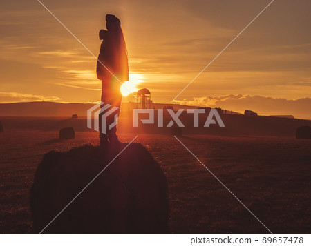 Silhouette of a girl standing on a haystack in a field high in the mountains against the backdrop of the setting sun 89657478