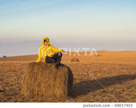A woman sits on a haystack in a high-altitude autumn field. Travel through the countryside of the Caucasus A woman sits on a haystack in a high-altitude autumn field. Travel through the countryside of the Caucasus 89657483