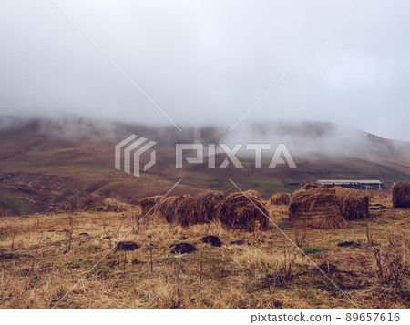Hills covered with autumn dried grass with haystacks and fog descending on a cloudy day. Countryside area. Highlands of the Caucasus Hills covered with autumn dried grass with haystacks and fog descending on a cloudy day. Countryside area. Highlands of the Caucasus 89657616
