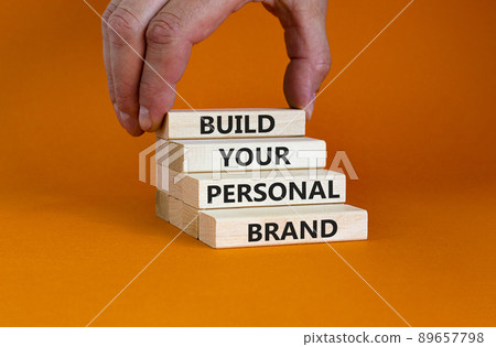 Build your personal brand symbol. Concept words Build your personal brand on wooden blocks. Businessman hand. Beautiful orange background. Build your personal brand business concept. Copy space. Build your personal brand symbol. Concept words Build your personal brand on wooden blocks. Businessman hand. Beautiful orange background. Build your personal brand business concept. Copy space. 89657798