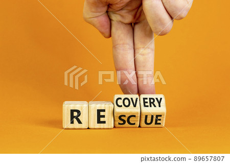 Recovery and rescue symbol. Businessman turns cubes and changes the word 'recovery' to 'rescue'. Beautiful orange background. Business and recovery - rescue concept. Copy space. Recovery and rescue symbol. Businessman turns cubes and changes the word 'recovery' to 'rescue'. Beautiful orange background. Business and recovery - rescue concept. Copy space. 89657807