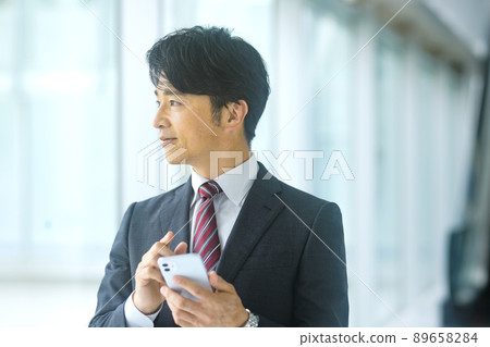 A middle-class businessman in a suit who operates a smartphone in the office 89658284