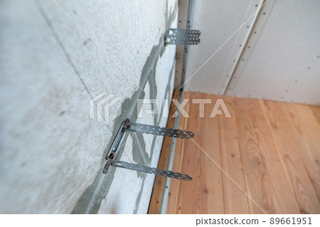 Unfinished brick wall in a room under construction prepared for drywall plates frame installation. Unfinished brick wall in a room under construction prepared for drywall plates frame installation. 89661951