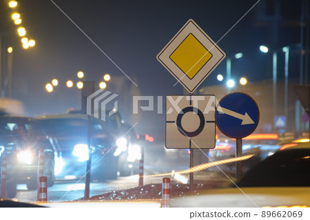 Roundabout road signs with blurred cars on city street traffic at night. Urban transportation concept Roundabout road signs with blurred cars on city street traffic at night. Urban transportation concept 89662069