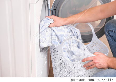 A man takes dried bed linen out of the dryer A man takes dried bed linen out of the dryer 89662117